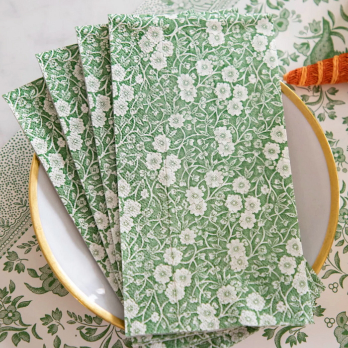 A stack of Hester & Cook Green Calico Paper Guest Towels (16 pack) with a white floral pattern rests on a plate with a yellow rim, while the background mirrors the elegant design for a cohesive, stylish look.