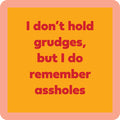 The Grudges Coaster by Drinks On Me features bold red text—“I don’t hold grudges, but I do remember assholes”—on an orange background with a peach border. Great for funny drink coaster designs or quirky bar cart accessories.