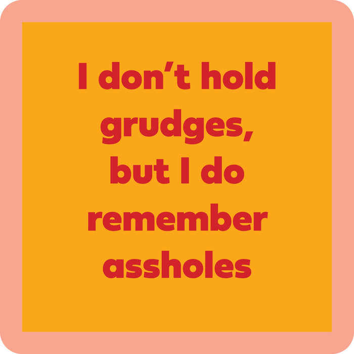 The Grudges Coaster by Drinks On Me features bold red text—“I don’t hold grudges, but I do remember assholes”—on an orange background with a peach border. Great for funny drink coaster designs or quirky bar cart accessories.