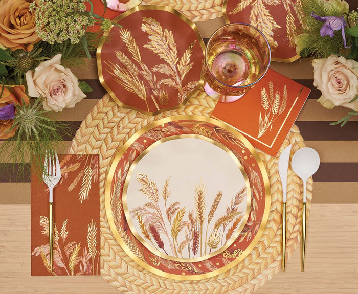 Create an elegant table setting with Sophistiplate’s Harvest Wheat Salad Plates (8pk), featuring wavy edges, wheat-inspired designs, and gold trim. Complement the look with gold utensils, a gold-rimmed glass, orange napkins, and floral accents. A woven round placemat ties together the warm autumn colors of the arrangement. These disposable plates offer effortless cleanup without compromising on style.