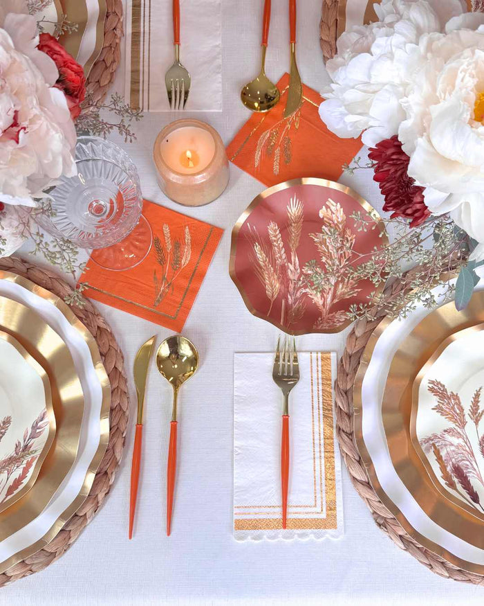 Create a stunning tablescape with the Sophistiplate Harvest Wheat Table Setting—designer disposable plates, orange napkins, gold cutlery, woven placemats, white tablecloth, crystal glasses, candlelight, and white peony florals—all in one party-in-a-box.