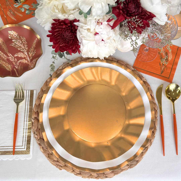 The Harvest Wheat Table Setting by Sophistiplate features designer disposable plates, orange-handled cutlery, orange napkins, a woven placemat, a copper dish, and a floral centerpiece for a stylish party-in-a-box look.