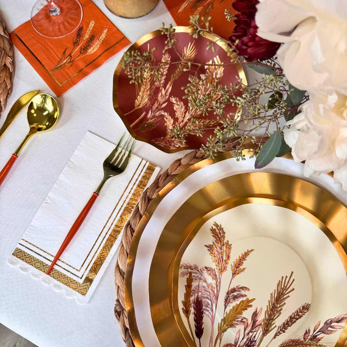 The Harvest Wheat Table Setting by Sophistiplate features gold-rimmed plates, red-handled utensils, fall-themed designer disposables, decorative flowers, and a woven placemat for an elegant autumn-inspired arrangement.