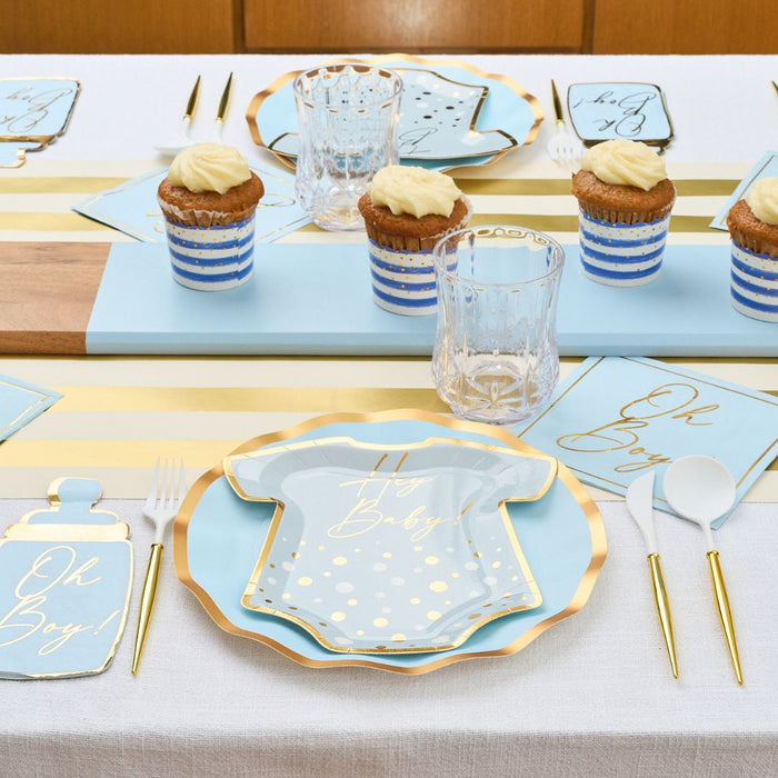 The Hey Baby Blue Table Setting by Sophistiplate LLC features blue and gold “Oh Boy!” onesie-shaped plates, striped cupcake wrappers, napkins, and gold-accented cutlery on a white tablecloth—perfect for baby showers.