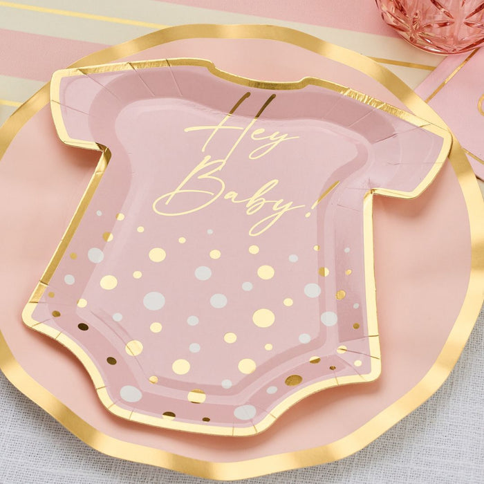 The Hey Baby Blush Table Setting by Sophistiplate LLC features a pink onesie-shaped plate with gold polka dots and trim, reading "Hey Baby!" in gold script—perfect for a chic baby shower celebration.