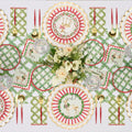 A festive Christmas table features red, gold, and green reindeer and monogram plates, gold utensils, crystal glasses, and a centerpiece of white calla lilies and roses on the Rosanne Beck Holly Berry Trellis Table Runner (20x12").