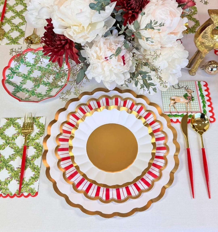 Create a festive holiday tablescape with the Holly Berry Table Setting by Sophistiplate—designer red, white, and gold scalloped plates, gold cutlery with red handles, themed napkins, and a centerpiece of white and red flowers with greenery.