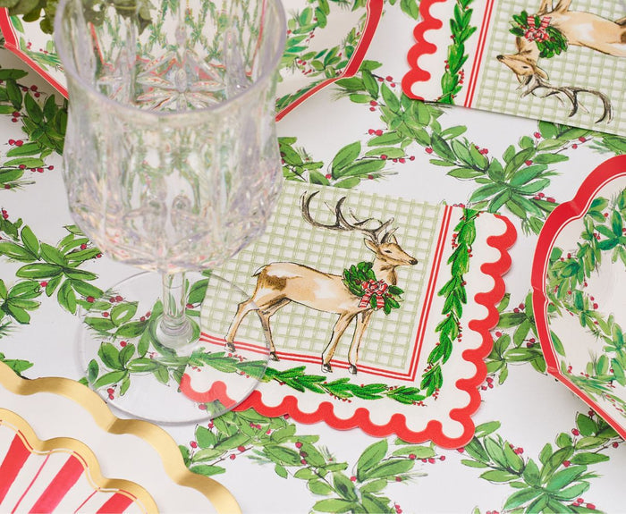 Create a charming Christmas table with a clear glass, plates, and napkins adorned with a reindeer and festive foliage, all set on the Rosanne Beck Holly Berry Trellis Table Runner (20x12") for an inviting holiday look.