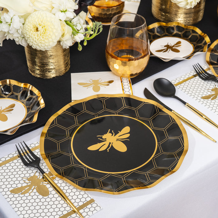 Elegant party tableware sets the scene, with Sophistiplate’s Honeybee Appetizer/Dessert Bowls at each place setting—each bowl featuring a striking honeybee motif. Matching cutlery, napkins, and honeycomb-patterned accents complete the bee-themed decor. White flowers in gold vases decorate the table.