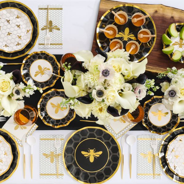 Sophistiplate Honeybee Dinner Plates (8-pack) create an elegant table setting with their black, white, and gold ruffled edges and charming honeybee design, beautifully paired with honeycomb patterns, gold flatware, a floral centerpiece, refreshing drinks, and sliced limes arranged on a wooden board.