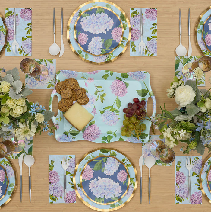 The Hydrangea Table Setting by Sophistiplate includes designer floral plates, matching napkins, a serving tray, and is arranged for four with cheese, crackers, grapes, white flowers in vases, forks, spoons, and clear glasses.