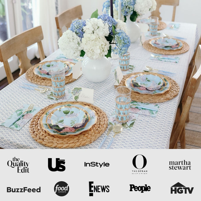 The Hydrangea Table Setting by Sophistiplate features woven placemats, floral designer disposable plates, gold cutlery, blue-patterned glasses, and white vases with blue and white hydrangeas. Media logos are displayed at the bottom.