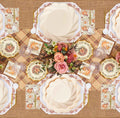 Enjoy a festive tablescape with the Sophistiplate Ivory Harvest Table Setting, featuring floral centerpieces, eco-friendly disposable plates adorned with pumpkin illustrations, a plaid table runner, gold utensils, glasses, and napkins—all elegantly arranged on a burlap tablecloth.