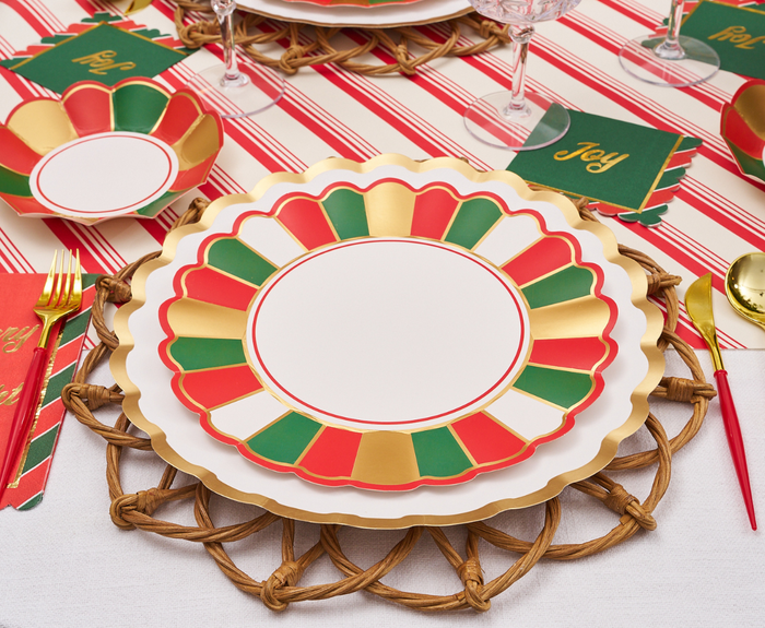 A festive table features Sophistiplate Joyful Christmas Dinner Plates/8pk with scalloped edges, gold flatware, Joy napkins, and a red-and-white striped tablecloth for a complete holiday look.