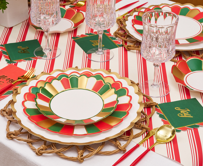 A festive table features Sophistiplate’s Joyful Christmas Salad Plates (8pk), crystal glasses, gold cutlery, “Joy” napkins, red chopsticks, woven placemats, and a red-and-white striped tablecloth.