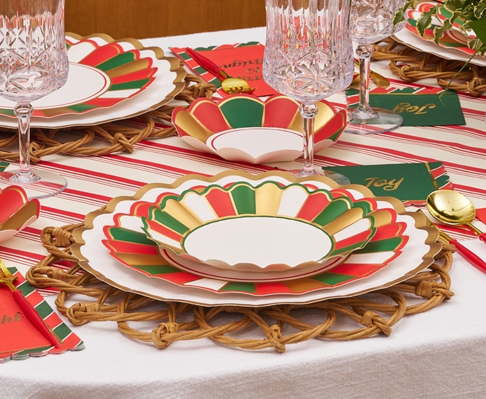 A festive table is set with Sophistiplate Joyful Christmas Salad Plates (8pk), crystal glasses, gold utensils, woven placemats on a striped cloth, and holiday cards with "Joy" and greenery for a cheerful touch.