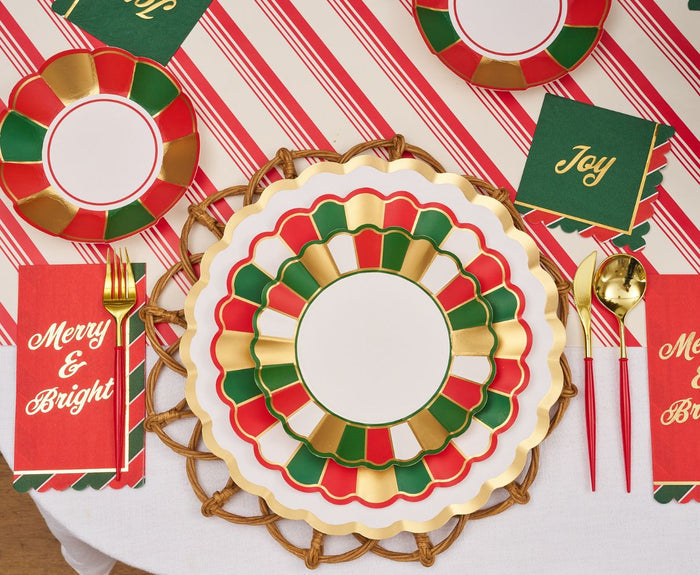 The Joyful Christmas Table Setting by Sophistiplate includes red, green, white, and gold scalloped plates, gold utensils, Merry & Bright napkins, Joy cards, and a candy cane striped tablecloth—perfect for festive holiday parties.