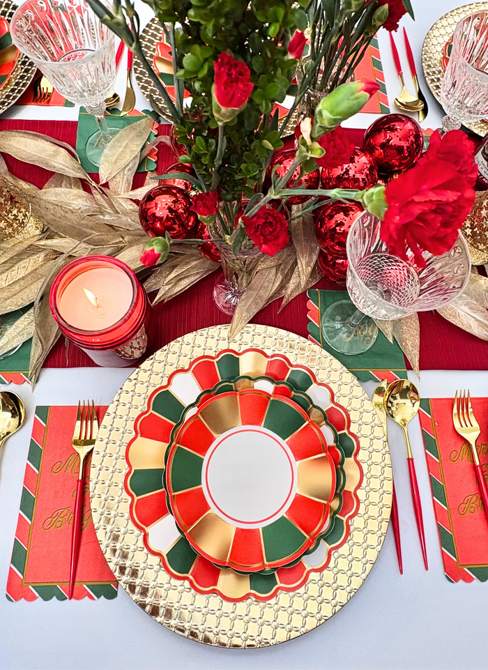 Create a Joyful Christmas Table Setting by Sophistiplate with red, green, and gold scalloped disposable plates, gold chargers and cutlery, crystal glasses, festive candles, carnations, ornaments, and holiday placemats—perfect party supplies!.
