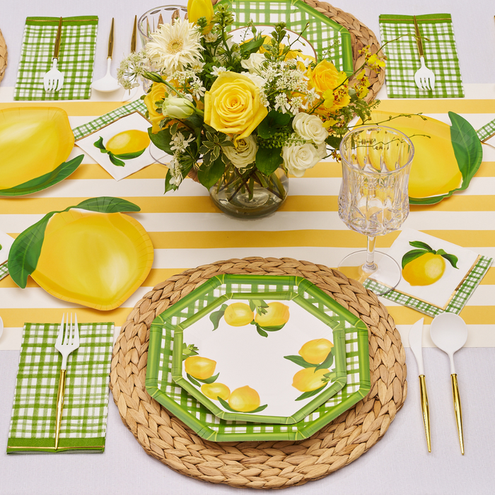 The Lemon and Stem Table Setting by Sophistiplate includes lemon-themed plates, green plaid napkins, white cutlery with gold handles, a woven placemat, yellow striped runner, and a cheerful bouquet of yellow and white flowers.