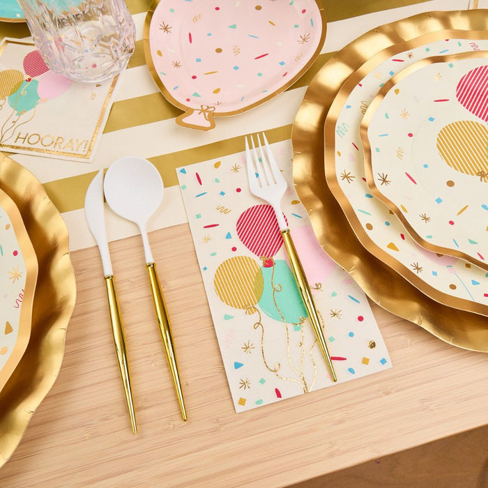 The Let's Celebrate Table Setting by Sophistiplate features designer disposable plates, gold-rimmed cutlery, balloon-patterned napkins, and confetti-themed plates set on a striped runner for a festive tablescape.