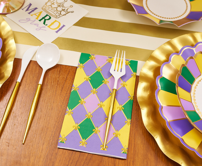 The Let's Mardi Table Setting by Sophistiplate features designer plates, a fleur-de-lis napkin, white utensils with gold handles, and purple, green, and gold decor for a festive Mardi Gras look.