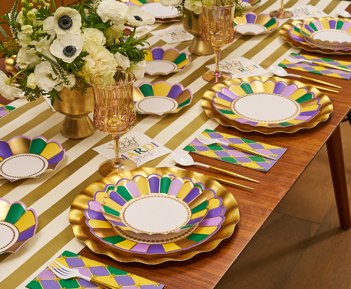 Create a festive tablescape with the Let's Mardi Table Setting by Sophistiplate, featuring vibrant designer plates, themed napkins, a striped runner, gold cutlery, and floral accents—perfect for celebrating in style.
