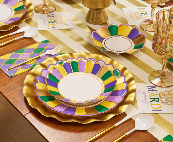The Let's Mardi Table Setting by Sophistiplate features gold, purple, green, and white designer plates, gold cutlery, festive napkins, and Mardi Gras cards on a striped runner—creating a stunning disposable Mardi Gras tablescape.