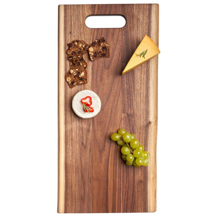 The Maple Live Edge Walnut Single Handle Charcuterie Board (24" x 12") displays a cheese wedge, soft cheese with red pepper slices, seed crackers, and green grapes arranged neatly on top.