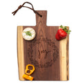 The Maple Live Edge Walnut Single Handle Charcuterie Board (9" x 6") features a “joy” wreath engraving, is styled with round cheese, strawberry, bell pepper slices on top, and includes a leather loop on the handle.