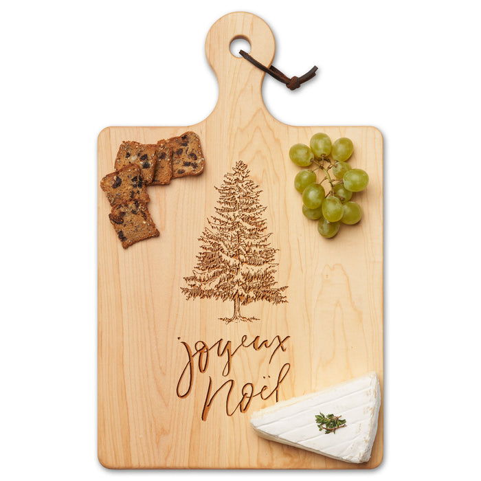 The Maple Maple Wood Cutting & Cheeseboard | Joyeux Noel | 16 x 10" features an engraved “Joyeux Noël” and tree design, beautifully presented with green grapes, crackers, and a wedge of cheese.