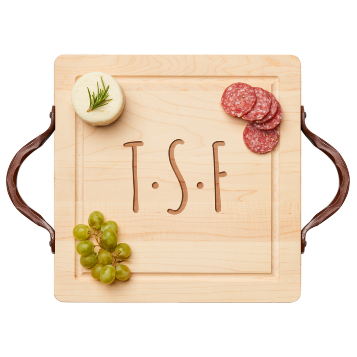 The Maple 12x12" Square Maple Wood Cutting & Cheeseboard with traditional handles, personalized with initials T.S.F., holds green grapes, rosemary-topped round cheese, and salami slices.