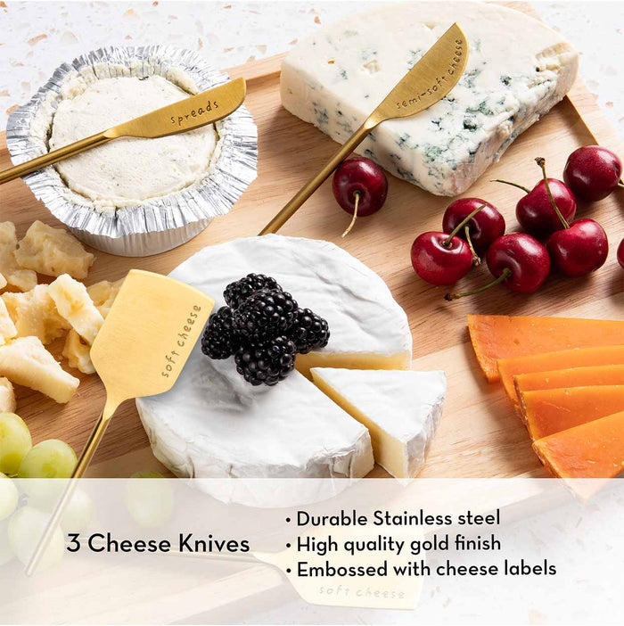 The Meg Quinn Charcuterie Board & Accessories Kit by Maple displays cheeses, cherries, and grapes with three gold knives labeled spreads, stirring cheese, and soft cheese. The set highlights unique knife features for perfect serving.