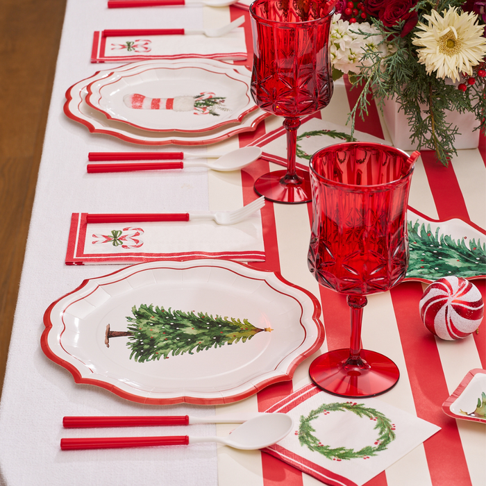 A Merry and Bright table setting features Sophistiplate's Merry and Bright Paper Dinner Plates (8pk), red and white striped runner, festive napkins, red glasses, matching utensils, and a floral centerpiece to complete your holiday look.