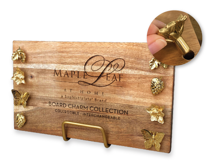 A wooden board engraved with "Maple," decorated with gold leaf and butterfly charms on the edges, rests elegantly on the Maple Metal Board Display Stand - Matte Gold. Inset: close-up of a magnetic gold charm.
