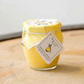 Bella Cucina's Meyer Lemon Spread comes in a glass jar covered with yellow paper and tied with string, featuring a lemon-illustrated label—ideal as a dessert topping.