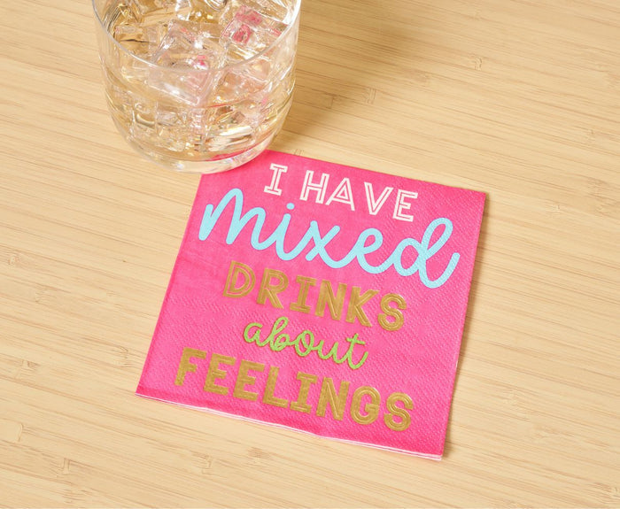A glass of iced beverage rests beside Sophistiplate’s ‘Mixed Drinks About Feelings’ Cocktail Napkins/26pk, featuring fun blue, white, and gold lettering—perfect for adding a playful touch to any happy hour.