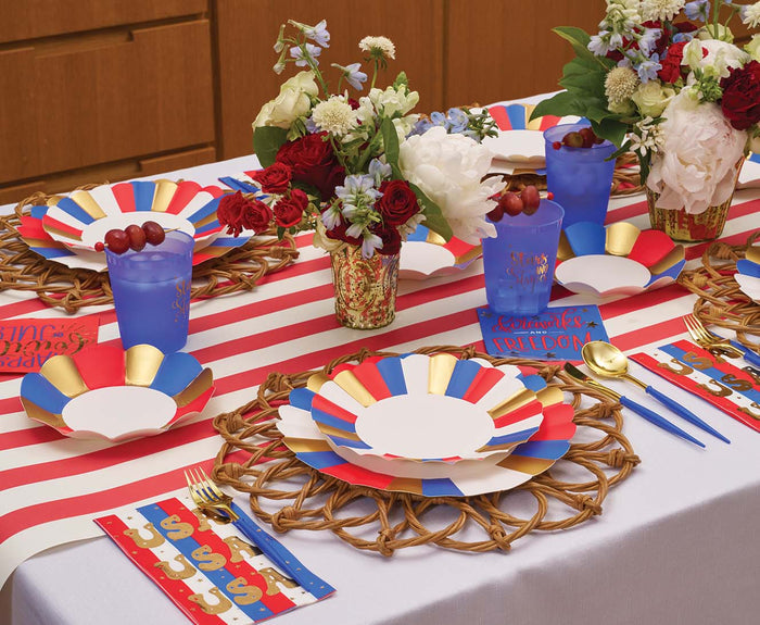 A festive table features Sophistiplate's Modern Patriotic Appetizer/Dessert Bowls (8pk), colorful plates, blue cups with red grapes, striped runners, gold accents, floral centerpieces, and decorative placemats for a patriotic-themed celebration.