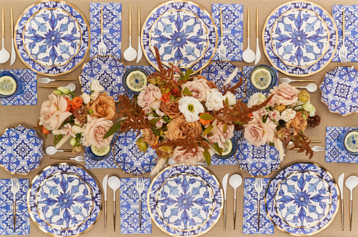 Create a stunning tablescape with the Moroccan Table Setting by Sophistiplate LLC, featuring blue and white patterned heavy duty plates, gold cutlery, white napkins, and peach and white roses on a burlap tablecloth.