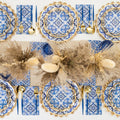 Overhead view of the Moroccan Table Setting by Sophistiplate LLC: a table for eight with blue and white heavy-duty paper plates, gold cutlery, blue napkins, beige lace placemats, and a dried grasses and pampas centerpiece.