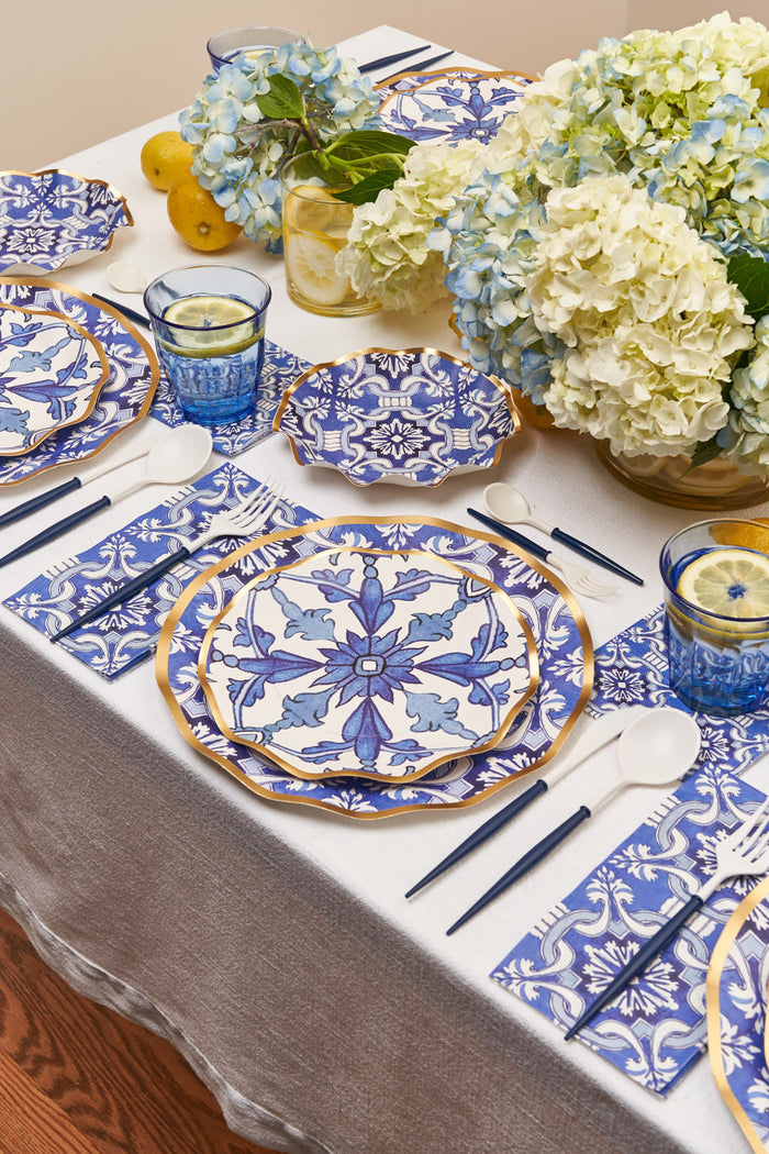 The Moroccan Table Setting by Sophistiplate LLC features blue and white patterned plates, gold chargers, blue glasses with lemon drinks, white cutlery, patterned napkins, hydrangea vases, lemons, and a white tablecloth for an elegant boxed party.