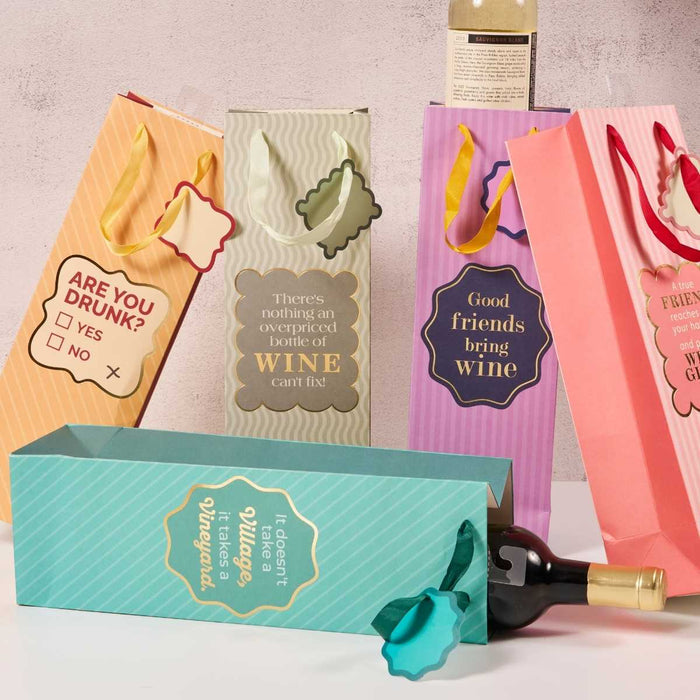 The Overpriced Bottle Wine Bag by Drinks On Me is a colorful, reusable gift bag with a humorous message, ribbon handle, and decorative tag—perfect as a stylish hostess gift. One bag is shown upright, another with a wine bottle partially outside.