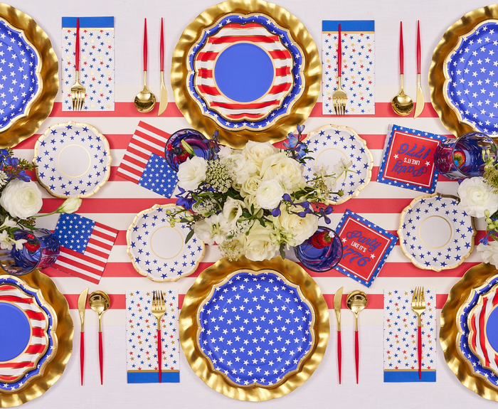 A festive table set with Sophistiplate's Party in the USA Guest Towels, themed plates and cups, gold cutlery, and red, white, and blue decor. White flowers and mini American flags complete this patriotic party look.