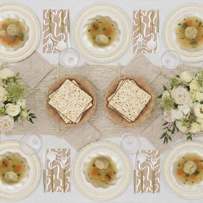 Set a festive Passover table for 16 with the Stunning Seder by Sophistiplate LLC, featuring matzah, matzo ball soup bowls, wine glasses, white flowers, beige napkins on a woven runner, and eco-friendly party plates.