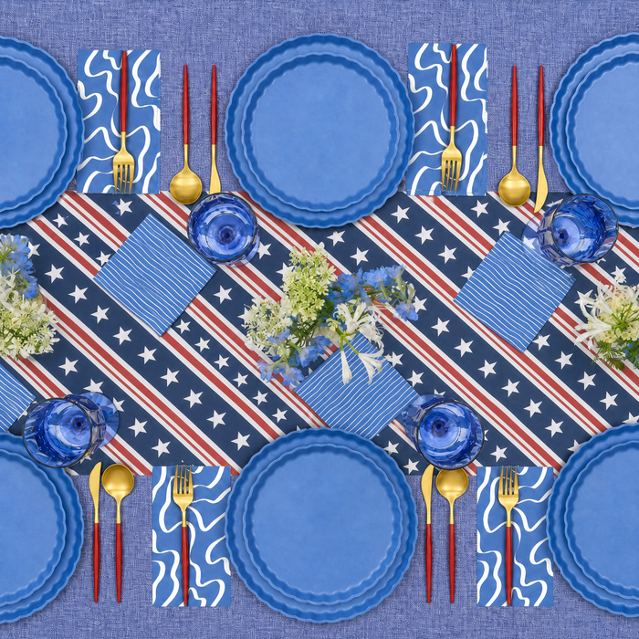 Celebrate with Sophistiplate's 4th of July Table for 16+ in French Blue—includes eco-friendly plates, gold cutlery, blue glassware, and a star-spangled runner with matching floral centerpiece for a festive holiday setting.