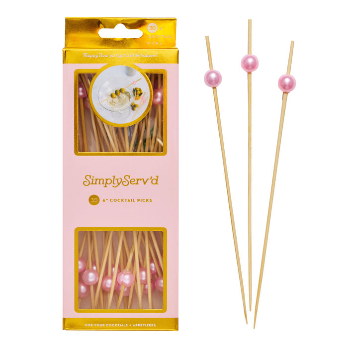 A pink and gold Simply Serv'd box labeled "Pearl Pink 6\" Wood Party Pick/30pk" contains 30 compostable wood party picks with pink pearl-like beads. Three large picks are displayed next to the box.
