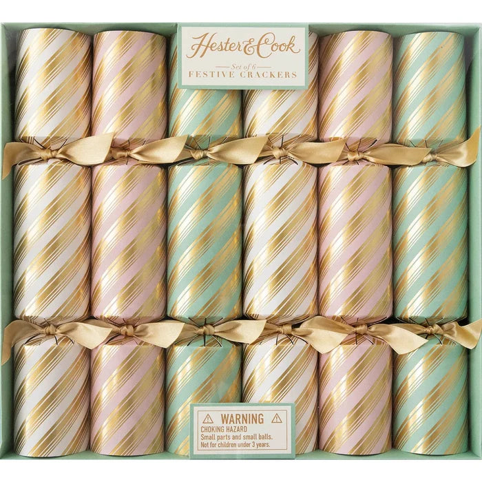 A box of twelve Peppermint Stripe Crackers by Hester & Cook in pastel pink, gold, and teal with diagonal gold stripes and gold ribbons; includes a choking hazard warning on the label.