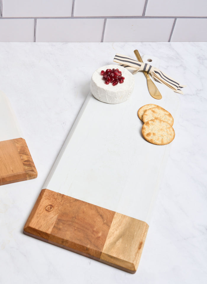 The Maple Personalized Acacia Bevel Board in white (20" x 7" x .6") holds cheese with pomegranate seeds, three crackers, and a gold knife tied with ribbon on a white countertop—an elegant choice for your charcuterie board spread.