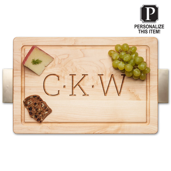 The Personalized Maple Wood Cutting + Cheeseboard 18 x 12" by Maple features metal handles and engraved initials "C K W." The board displays cheese with dill, green grapes, and bread, with a “Personalize this item!” label in the top right corner.