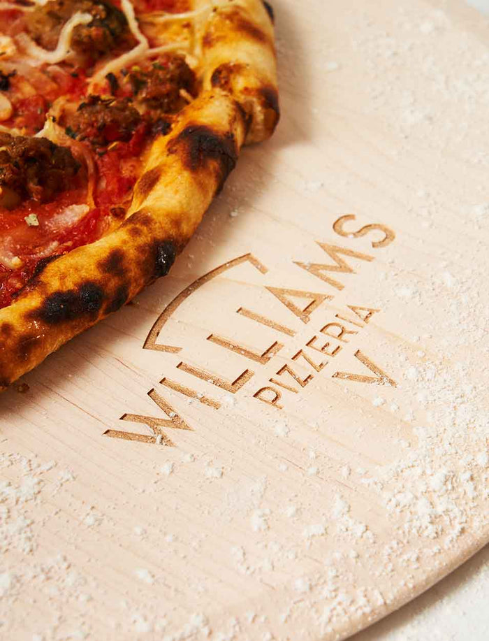 A golden, bubbly pizza sits on the Personalized Maple Wood Pizza Peel 14 x 21" by Maple, its surface lightly dusted with flour.