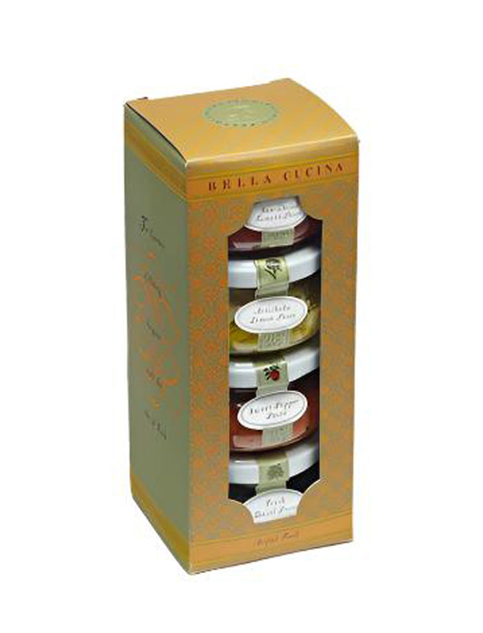 The Bella Cucina Piccolo Pesto Gift Collection features four stacked jars of popular pesto spreads, visible through a clear window on the gold and orange packaging.